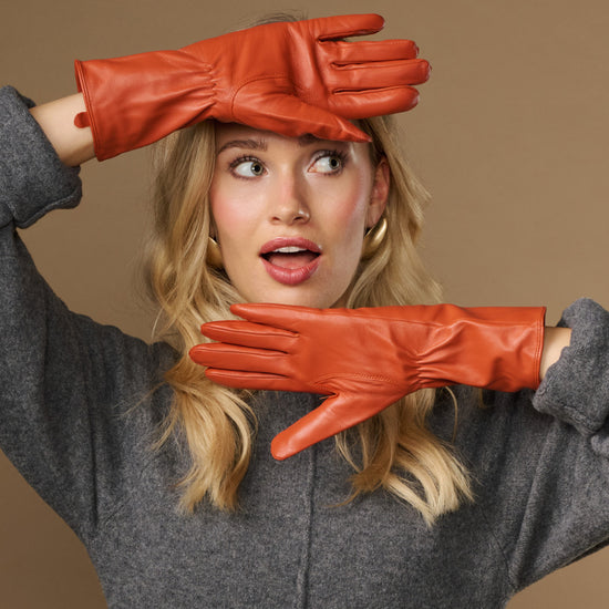 Orange leather gloves worn with hands raised; long sleeves and seam details