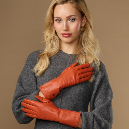 Orange leather gloves on hands with long cuffs and snug fit at wrists