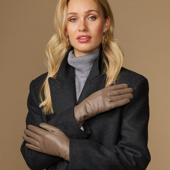 Pair of women’s taupe leather gloves with stitched seams, worn with dark outerwear