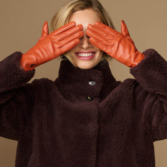 Lauren orange lambskin leather gloves with touchscreen tips, silk-lined, two hands raised