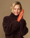 Lauren orange lambskin leather gloves with touchscreen tips, silk-lined, posed on hands