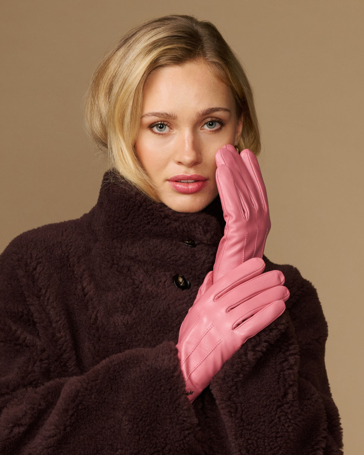 Pink leather gloves with dark fleece lining, hands held near face