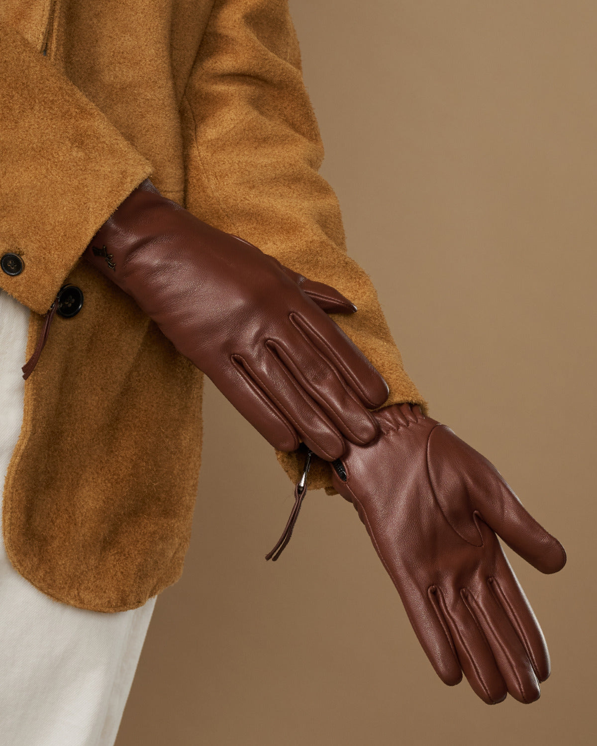 Close-up of brown leather gloves showing stitched seams and side zip
