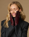 Women's black leather gloves with red-and-black checkered lining held near the face