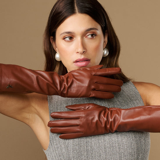 Cognac leather below-elbow gloves close-up, textured surface and fitted seams