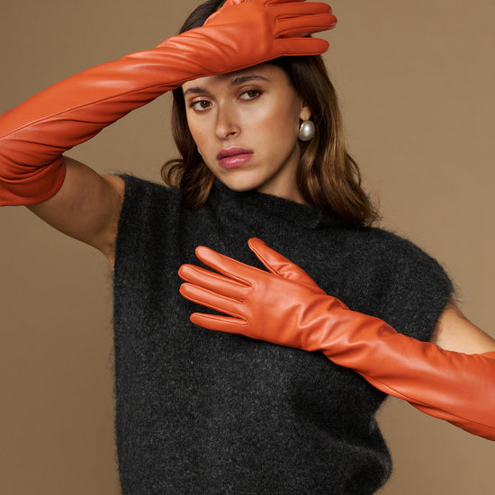 Orange lambskin leather gloves with silk lining and touchscreen tips, hands on head