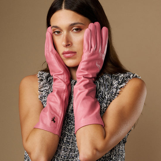 Pink women’s below-elbow leather gloves, fitted fingers, gloves held up near face