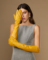 Yellow leather elbow gloves on model hands, one glove raised near face