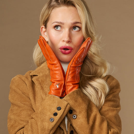Orange leather gloves with stitched fingers and soft lined cuffs, hands held at neck