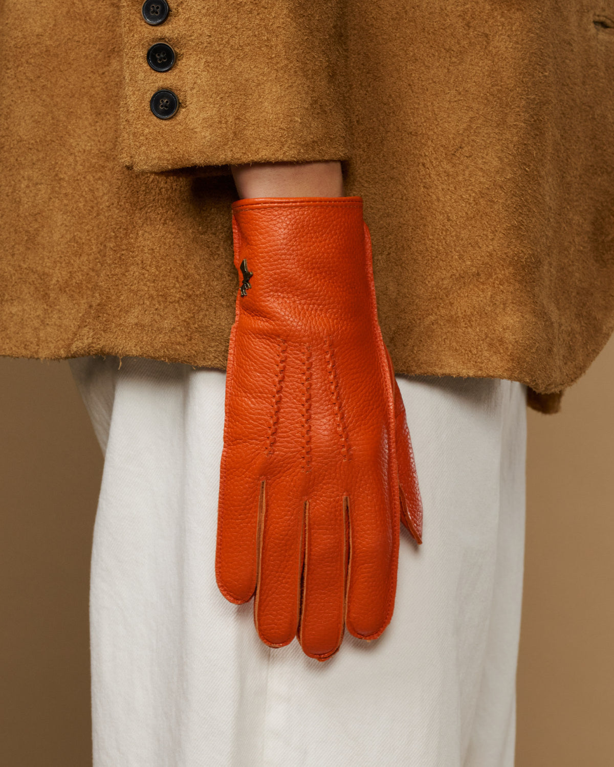 Orange leather glove with soft lined cuff and stitched fingertips, hanging from sleeve