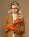 Orange leather gloves with stitched finger seams and soft cuff lining, worn with brown coat