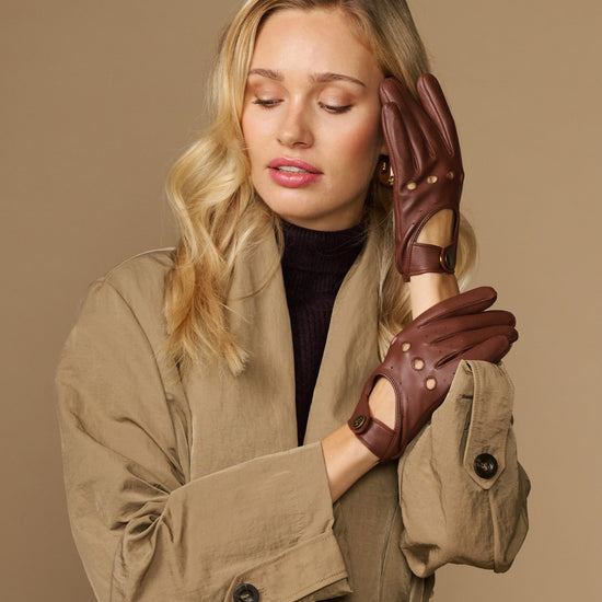 Brown leather driving gloves on model with elastic wrist and brass button cuff detail